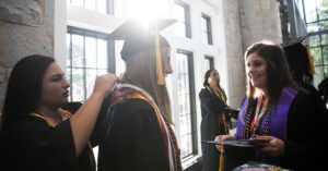 Women graduates help each other adjust stoles and cords before commencement.