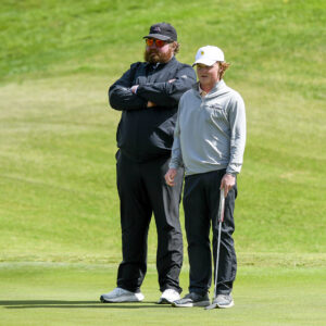 Eric Quinn stands next to a student athlete on the golf course,