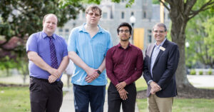 Four individuals stand together on the academic quad.