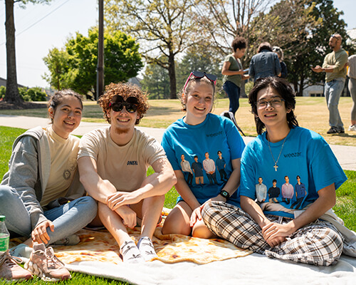 Friends sit on a blanket on the quad.